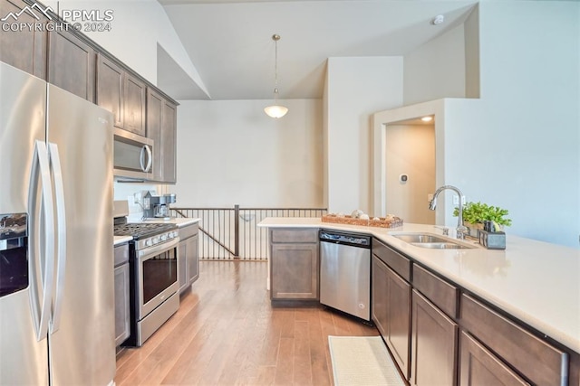 kitchen featuring sink, stainless steel appliances, pendant lighting, vaulted ceiling, and light hardwood / wood-style floors