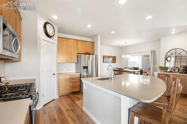 kitchen featuring appliances with stainless steel finishes, sink, a center island with sink, light hardwood / wood-style flooring, and hanging light fixtures