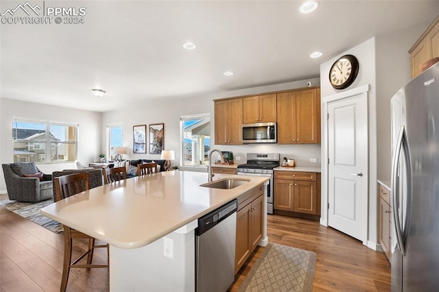 kitchen with hardwood / wood-style floors, a kitchen breakfast bar, stainless steel appliances, and a kitchen island with sink