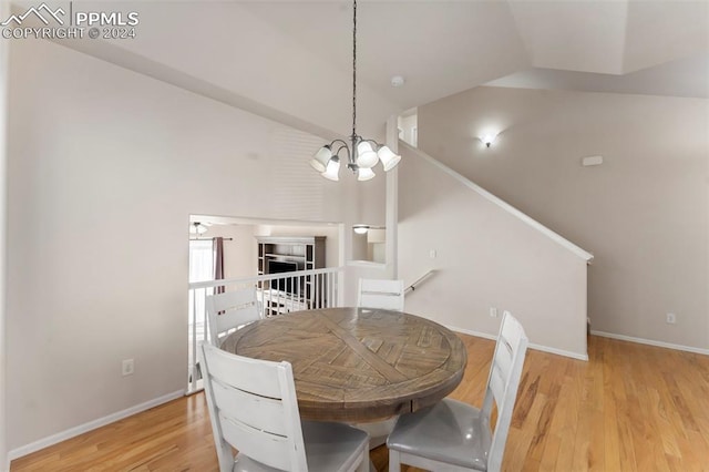 dining space with ceiling fan with notable chandelier, light hardwood / wood-style floors, and high vaulted ceiling