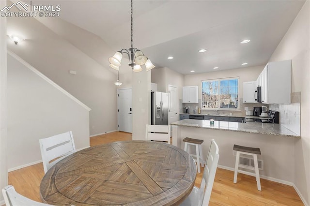 dining area with sink, light hardwood / wood-style flooring, lofted ceiling, and a notable chandelier