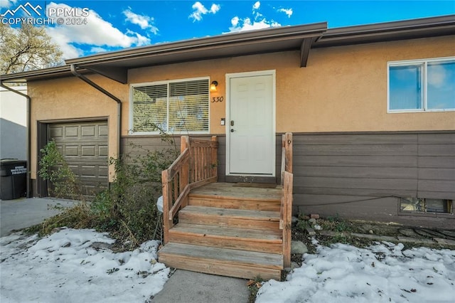 snow covered property entrance with a garage