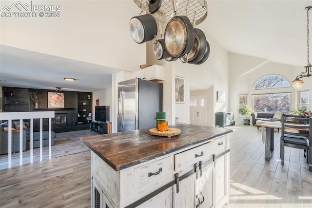 kitchen featuring light wood-type flooring, a towering ceiling, white cabinetry, a kitchen island, and stainless steel refrigerator