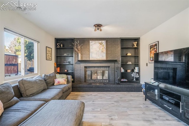 living room with built in shelves, light wood-type flooring, and a fireplace