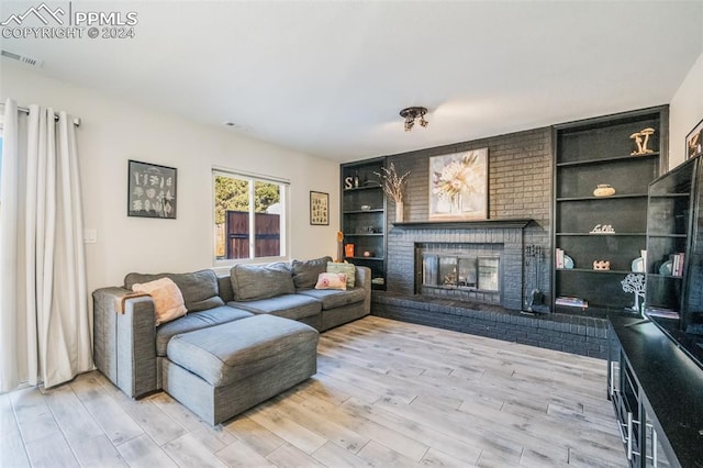 living room featuring built in features, light hardwood / wood-style floors, and a brick fireplace