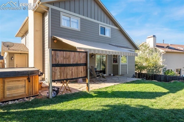 back of house featuring a hot tub, a patio area, and a lawn