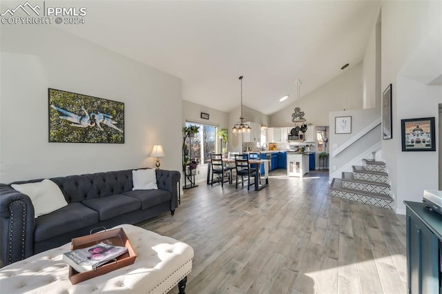 living room with light hardwood / wood-style floors, high vaulted ceiling, and a notable chandelier