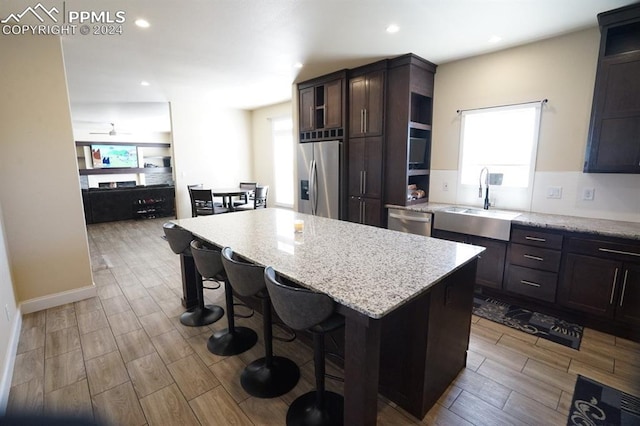 kitchen with a center island, sink, light hardwood / wood-style flooring, light stone countertops, and appliances with stainless steel finishes