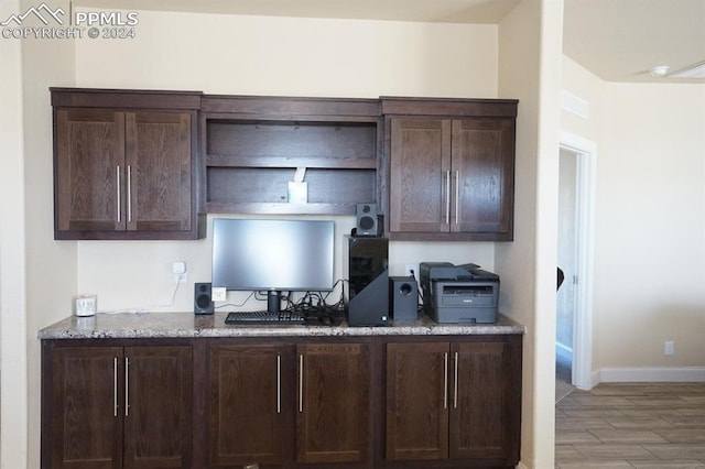 kitchen featuring light stone countertops, dark brown cabinets, and light wood-type flooring