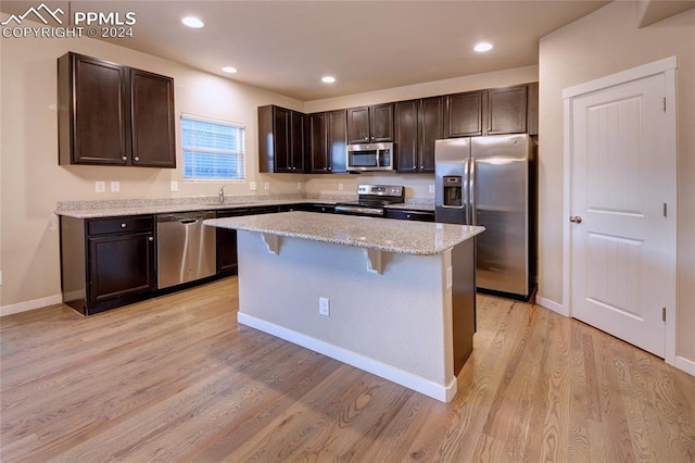 kitchen featuring light stone countertops, a kitchen breakfast bar, stainless steel appliances, a center island, and light hardwood / wood-style floors