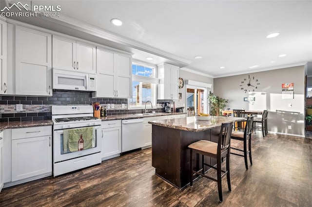 kitchen with white appliances, white cabinets, crown molding, dark stone countertops, and dark hardwood / wood-style flooring