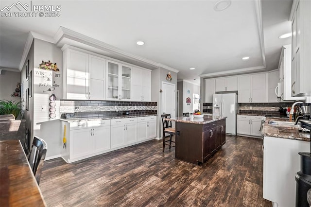 kitchen with white appliances, a kitchen island, dark stone countertops, dark hardwood / wood-style floors, and white cabinetry