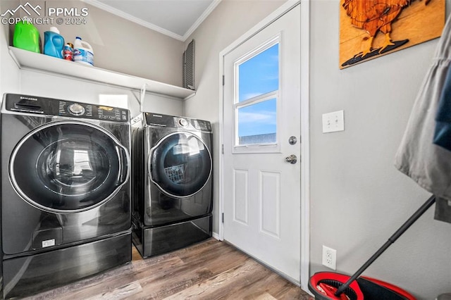 clothes washing area featuring washer and dryer, wood-type flooring, and ornamental molding