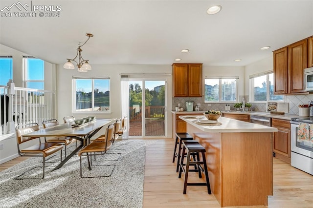 kitchen with decorative backsplash, stainless steel appliances, decorative light fixtures, light hardwood / wood-style floors, and a kitchen island