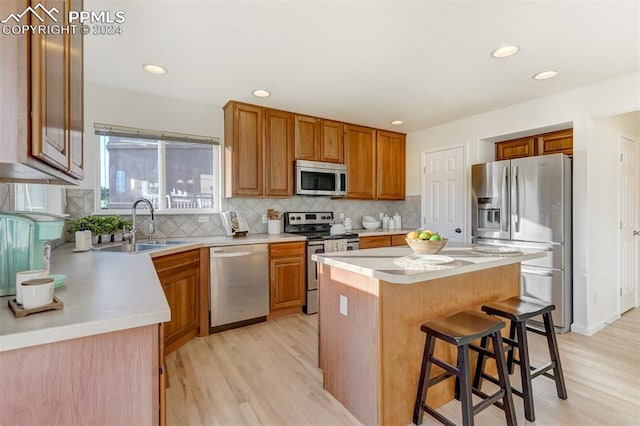 kitchen featuring a center island, sink, light hardwood / wood-style flooring, appliances with stainless steel finishes, and a kitchen bar