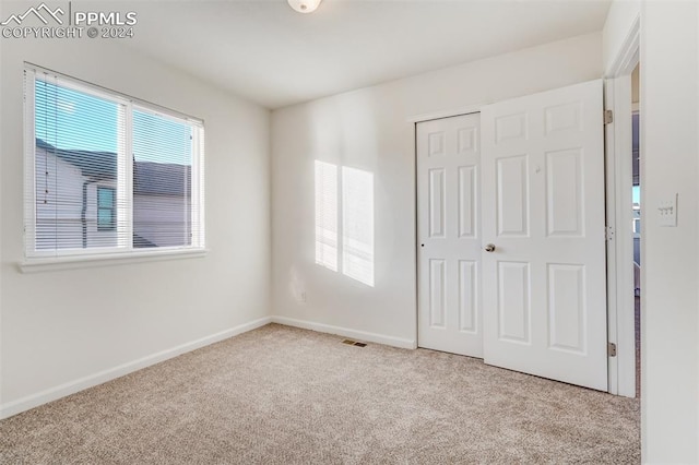 unfurnished bedroom with light colored carpet and a closet