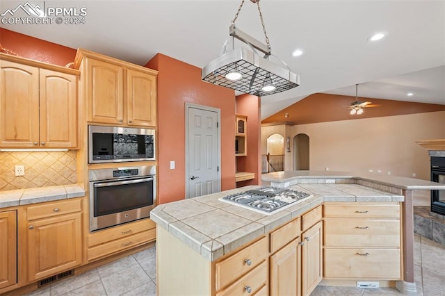 kitchen featuring ceiling fan, tile counters, lofted ceiling, a kitchen island, and appliances with stainless steel finishes