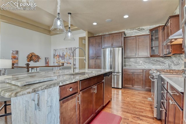 kitchen featuring a kitchen island with sink, sink, light hardwood / wood-style flooring, a kitchen bar, and stainless steel appliances