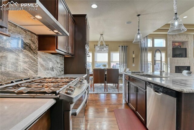 kitchen featuring wall chimney range hood, sink, appliances with stainless steel finishes, decorative light fixtures, and wood-type flooring