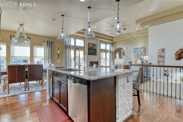 kitchen featuring stainless steel dishwasher, a center island with sink, sink, and light hardwood / wood-style flooring