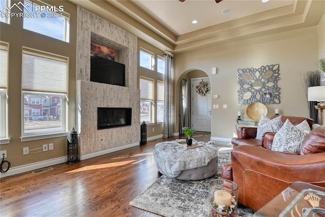 living room featuring a high ceiling, ceiling fan, a fireplace, a tray ceiling, and wood-type flooring