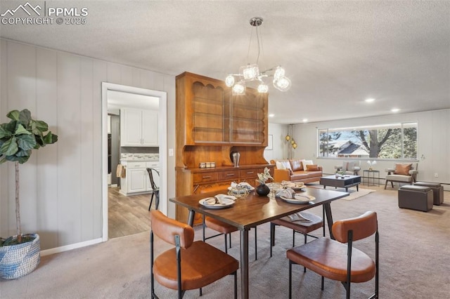 dining space with light colored carpet, a textured ceiling, and a notable chandelier