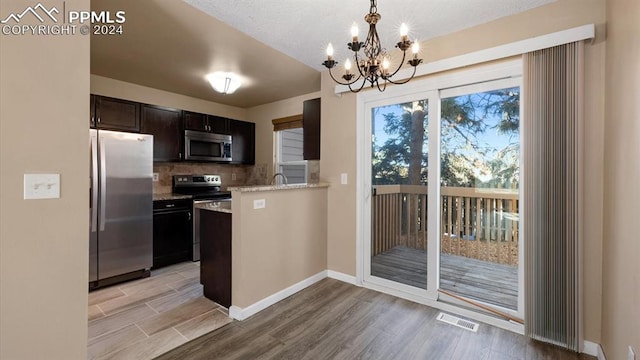 kitchen with decorative backsplash, appliances with stainless steel finishes, a chandelier, light hardwood / wood-style floors, and hanging light fixtures