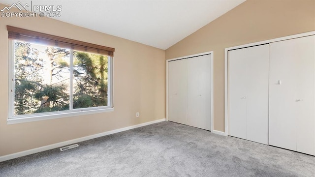 unfurnished bedroom featuring multiple closets, light carpet, and vaulted ceiling