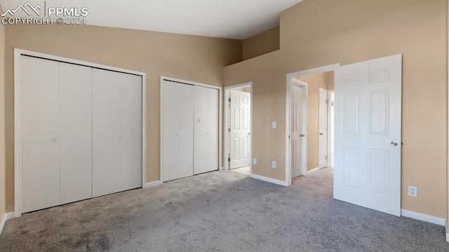 unfurnished bedroom with light carpet, high vaulted ceiling, and two closets