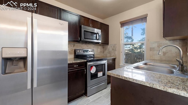 kitchen featuring decorative backsplash, appliances with stainless steel finishes, light stone counters, and sink