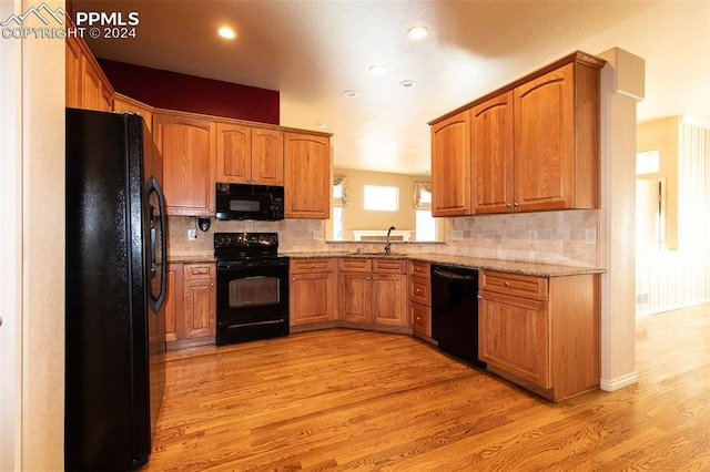 kitchen with light stone countertops, light wood-type flooring, tasteful backsplash, sink, and black appliances