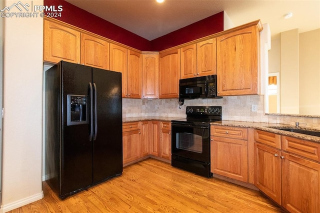 kitchen featuring sink, light stone counters, backsplash, light hardwood / wood-style floors, and black appliances