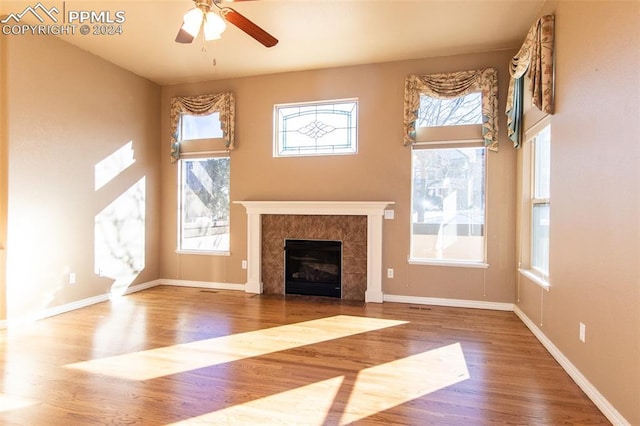 unfurnished living room featuring hardwood / wood-style flooring, ceiling fan, and a tiled fireplace