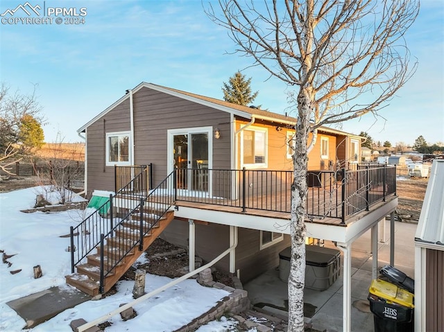 snow covered house with a wooden deck and a hot tub