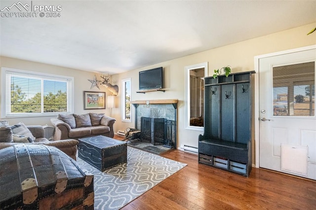 living room featuring a tiled fireplace, wood-type flooring, and a baseboard heating unit