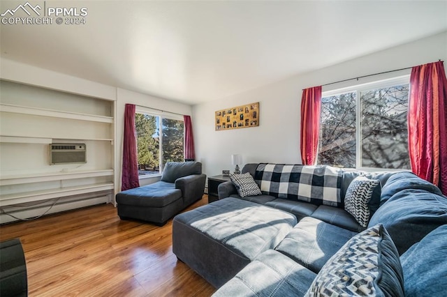 living room featuring a baseboard radiator, an AC wall unit, built in features, and wood-type flooring