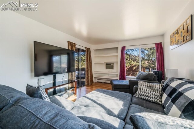 living room featuring an AC wall unit, hardwood / wood-style flooring, and built in shelves