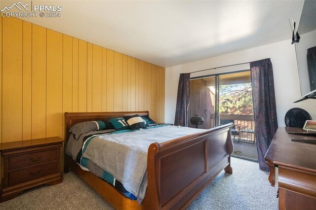 bedroom with wood walls, access to exterior, and light colored carpet