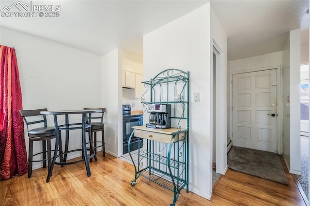 kitchen featuring white cabinetry, electric range, blue cabinetry, light hardwood / wood-style floors, and a kitchen bar