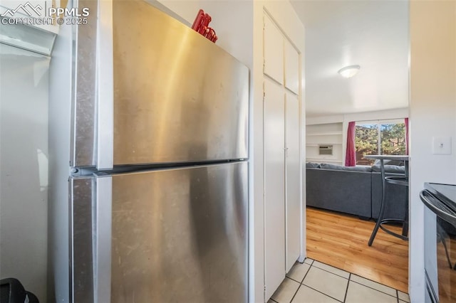 kitchen with light tile patterned flooring, white cabinetry, range with electric cooktop, and stainless steel fridge