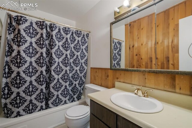 full bathroom with shower / bathtub combination with curtain, vanity, wood walls, and toilet