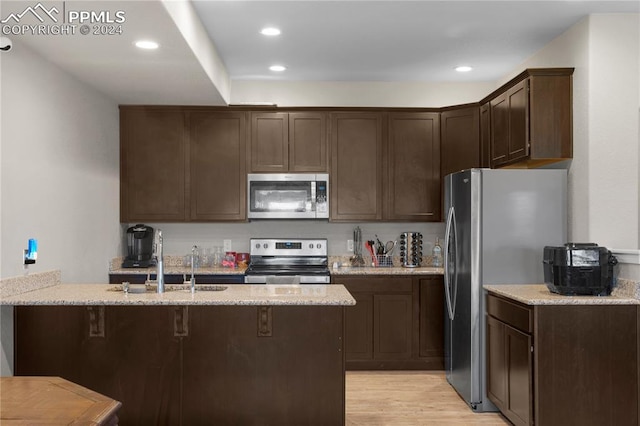 kitchen with dark brown cabinetry, light stone countertops, sink, stainless steel appliances, and light hardwood / wood-style flooring