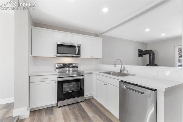 kitchen featuring kitchen peninsula, appliances with stainless steel finishes, backsplash, sink, and white cabinetry