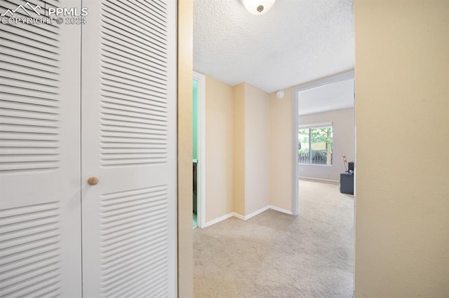 hallway featuring light carpet and a textured ceiling