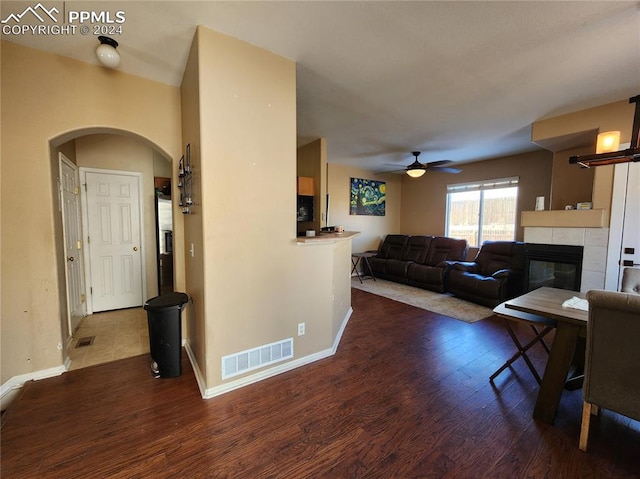 living room featuring ceiling fan, wood-type flooring, and a tiled fireplace