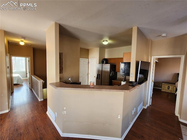 kitchen with kitchen peninsula, stainless steel refrigerator with ice dispenser, a textured ceiling, and dark wood-type flooring