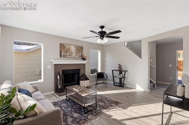 living room featuring a brick fireplace, ceiling fan, and light wood-type flooring