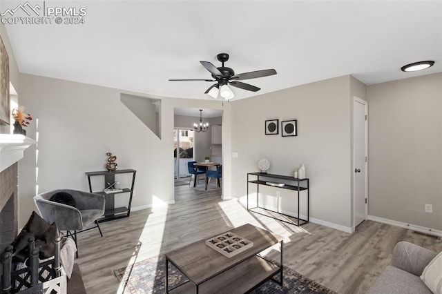 living room featuring a fireplace, light wood-type flooring, and ceiling fan with notable chandelier