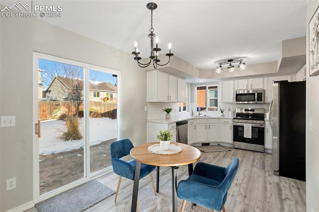 kitchen with appliances with stainless steel finishes, tasteful backsplash, light hardwood / wood-style flooring, white cabinetry, and hanging light fixtures