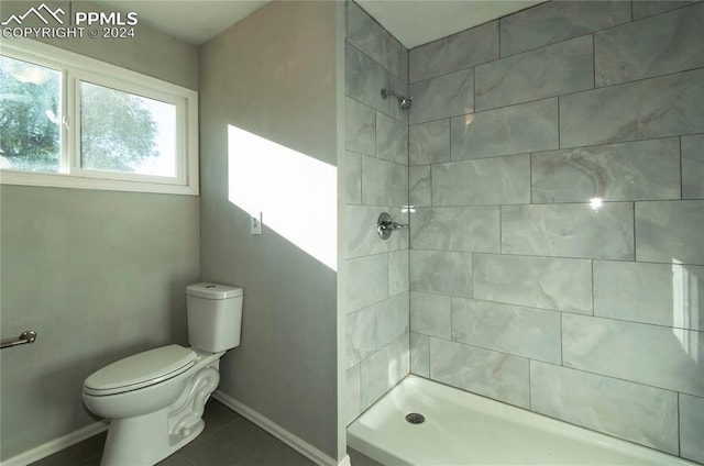 bathroom with tile patterned flooring, toilet, and a tile shower